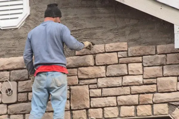 a man installing stone bricks on house