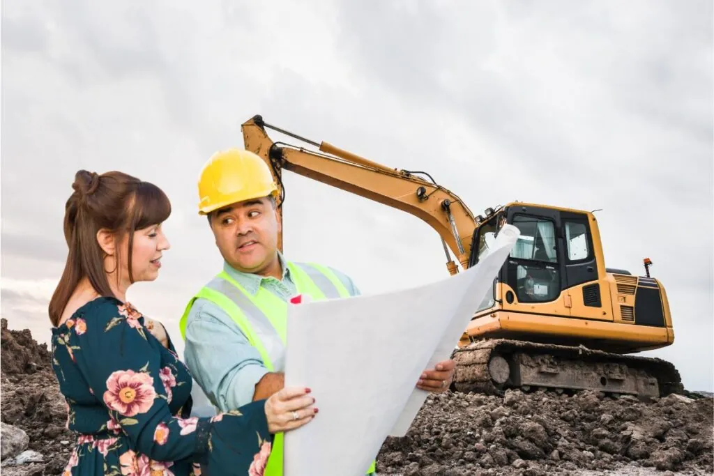 excavating male contractor talking with female client over blueprint